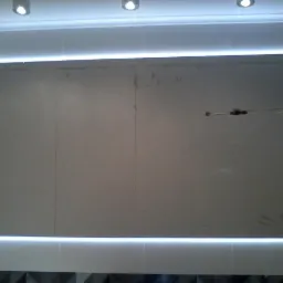 Ściana z płyt karton-gips z widocznymi śladami po instalacji elektrycznej, oświetleniem LED i fragmentem dekoracyjnej listwy przypodłogowej w łazience.