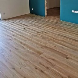 F.H.U. Żądlak - Ułożona jasna podłoga z desek w nowym pomieszczeniu z niebieską ścianą i otwartym przejściem do innego pokoju.