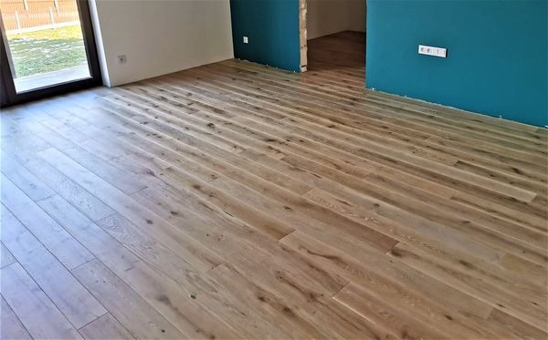 Ułożona jasna podłoga z desek w nowym pomieszczeniu z niebieską ścianą i otwartym przejściem do innego pokoju.