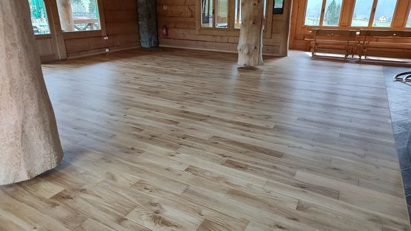 Jasne panele podłogowe z wyraźnym usłojeniem w przestronnym, drewnianym wnętrzu z pniem drzewa pełniącym rolę kolumny.