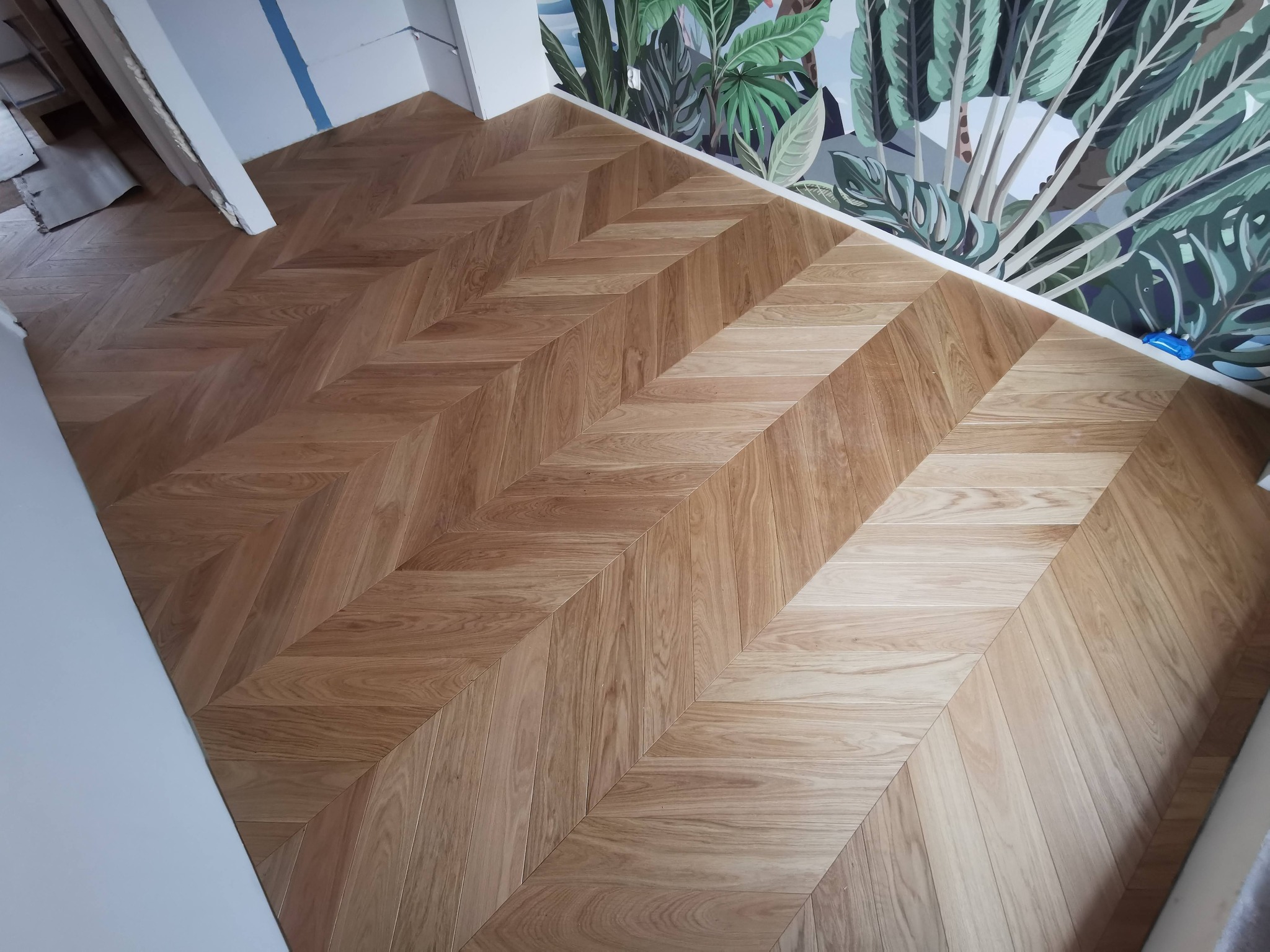 Parkiet ułożony we wzór jodełki w pomieszczeniu w Nowym Targu, widoczna ściana z tapetą w motywy roślinne.