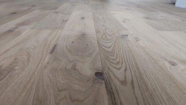 Jasna, dębowa podłoga z wyraźnym usłojeniem i naturalnymi sękami, sfotografowana pod kątem, ukazująca strukturę drewna.