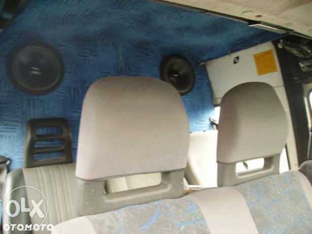 Wnętrze busa: szare fotele z zagłówkami na tle niebieskiej tapicerki z głośnikami. Widok z perspektywy pasażera.