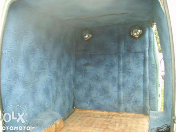 Wnętrze przestrzeni ładunkowej busa wyłożone niebieską tkaniną z widocznymi otworami wentylacyjnymi w górnej części ścian. Podłoga drewniana.