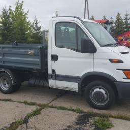 Składy węgla Pawłowski - Biały samochód dostawczy z otwartą skrzynią ładunkową na tle koparki i drzew. Widoczny model Iveco 50C13. Transport materiałów budowlanych lub opału.