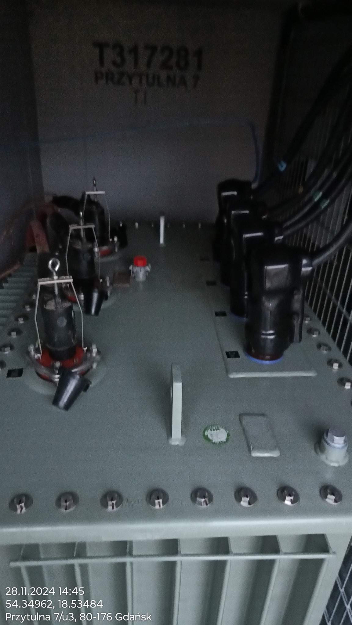 Wnętrze skrzynki elektrycznej z transformatorami i przewodami, widok z góry. Widoczne elementy instalacji i adres: Przytulna 7, Gdańsk.