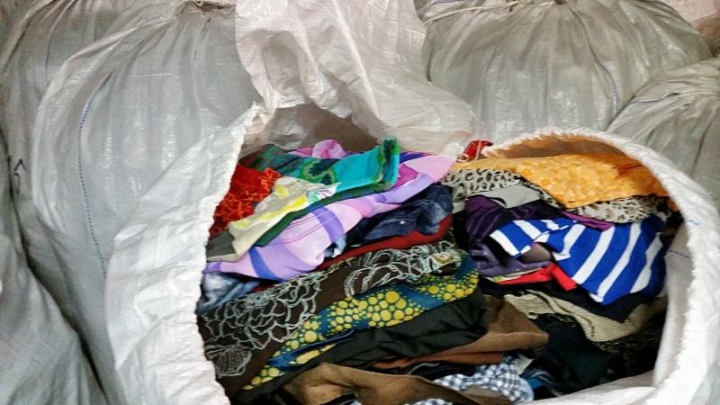 Worek z odzieżą używaną, wypełniony kolorowymi ubraniami o różnych wzorach i fakturach. Widoczne inne worki w tle, sugerujące dużą ilość zebranego asortymentu.