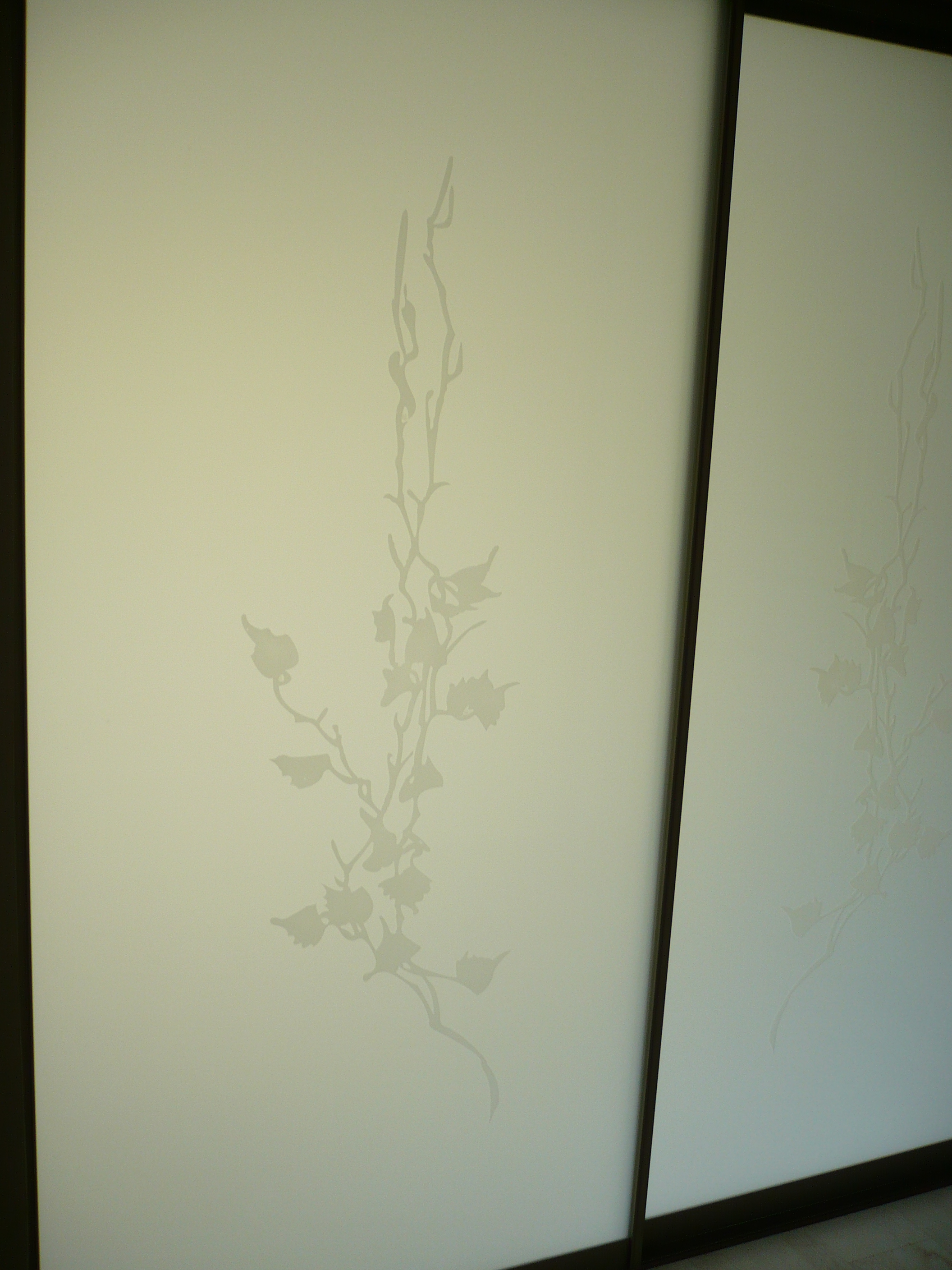 Białe drzwi przesuwne z motywem roślinnym, Częstochowa. Subtelny wzór na gładkiej powierzchni, minimalistyczny design, ciemne ramy.