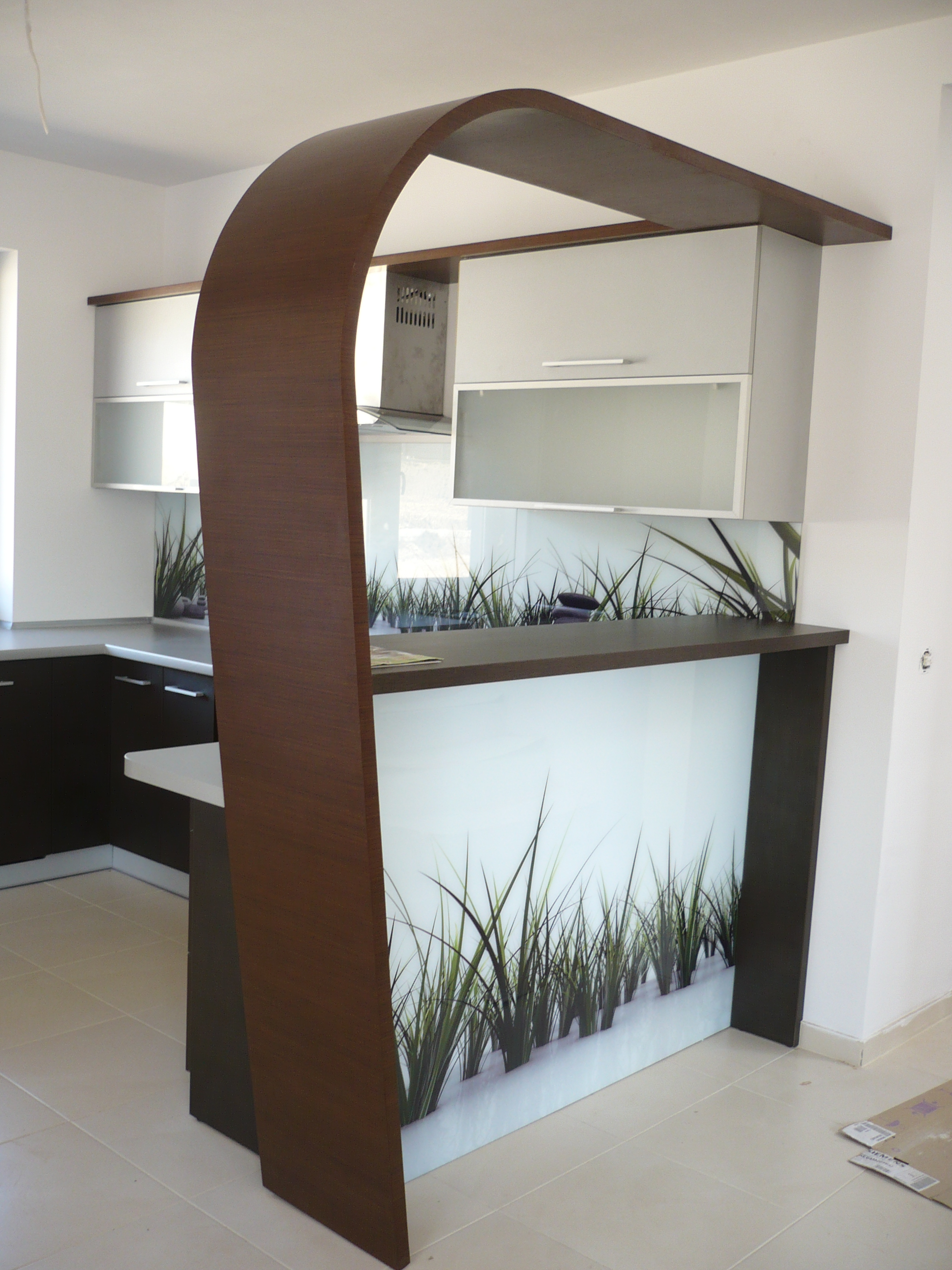 Nowoczesna kuchnia z barkiem i unikalną, łukową konstrukcją z drewna. Szklany panel z motywem trawy dodaje lekkości wnętrzu. Minimalistyczne szafki w jasnych kolorach.