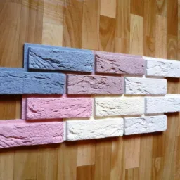 Dekoracyjne, kolorowe płytki imitujące cegłę ułożone na drewnianej podłodze. Odcienie niebieskiego, różu i bieli tworzą mozaikę. Widoczna faktura płytek.