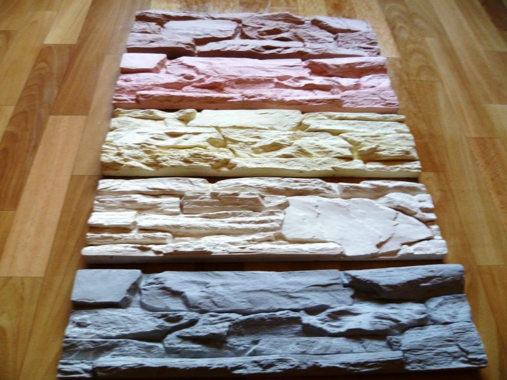 Panele dekoracyjne imitujące kamień w różnych odcieniach ułożone na podłodze z paneli drewnopodobnych. Prezentacja kolorystyki i faktury.