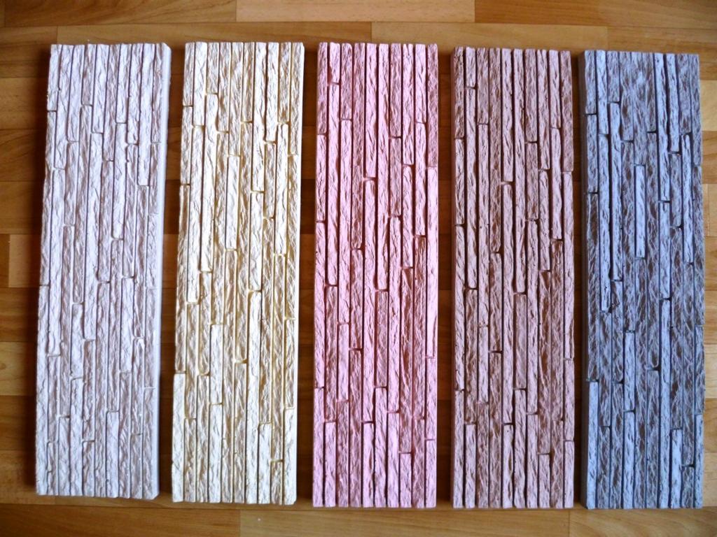 Próbki dekoracyjnych paneli ściennych w różnych odcieniach (biały, beżowy, różowy, brązowy, szary) ułożone na drewnianej podłodze. Prezentacja faktury i kolorystyki.