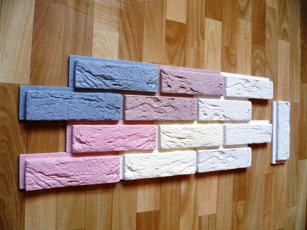 Dekoracyjne, kolorowe płytki imitujące cegłę ułożone na drewnianej podłodze. Odcienie niebieskiego, różu i bieli tworzą mozaikę. Widoczna faktura płytek.