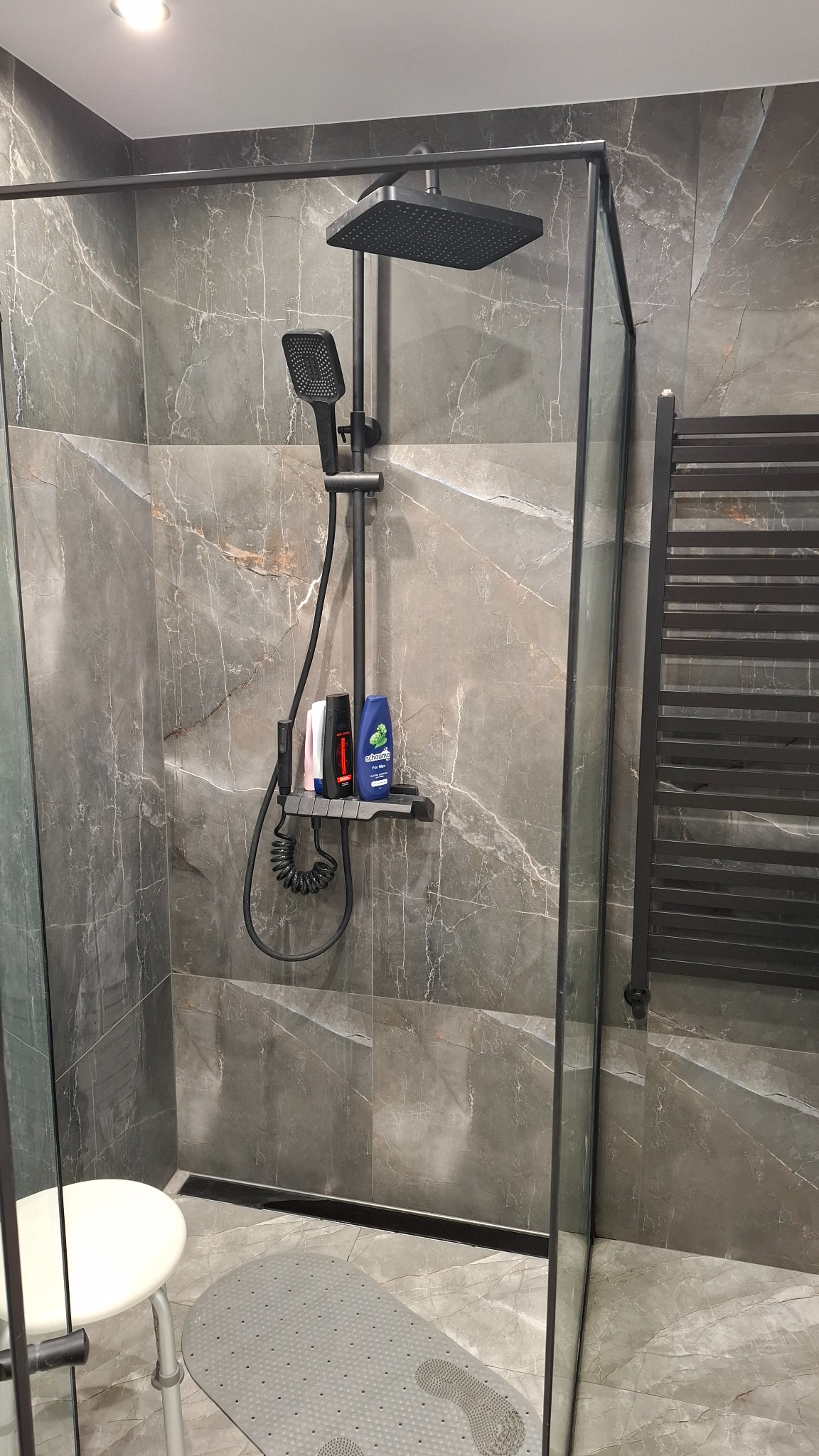 Kabina prysznicowa z czarną armaturą i marmurowymi płytkami w Stepnicy. Nowoczesny design, szklana ścianka i półka z kosmetykami pod prysznicem.