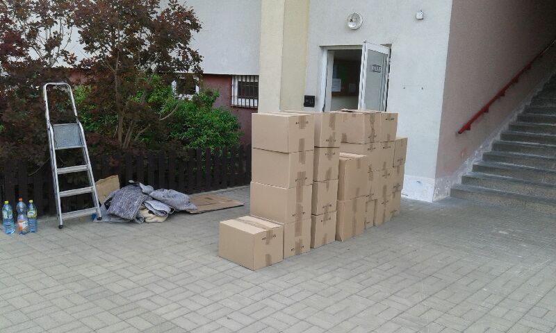 Stos kartonowych pudeł, drabina i zabezpieczenia przed budynkiem ze schodami. Przygotowania do przeprowadzki, widok z zewnątrz.