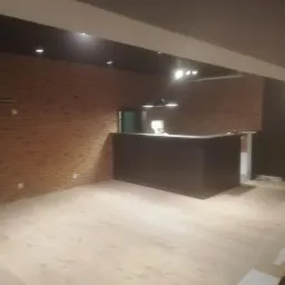 Wykończone wnętrze biurowe z ceglaną ścianą, drewnianą podłogą i ciemną ladą recepcyjną pod trzema lampami.