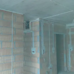 Surowe mury z cegły dziurawki z rozprowadzonymi przewodami elektrycznymi podtynkowo, widoczne puszki instalacyjne i przewody na suficie w nowym budynku.