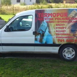 Biały samochód dostawczy z reklamą natrysku poliuretanem na dachy, stropy, ściany i fundamenty. Widoczny numer telefonu kontaktowego.