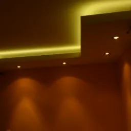 Oświetlony sufit podwieszany z halogenami, pomalowany na ciepły odcień, tworzący nowoczesny design wnętrza. Widoczna część okna i karnisza.