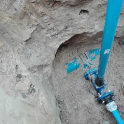 Niebieska rura wodociągowa z łącznikami w wykopie ziemnym, widoczne ślady świeżego montażu.
