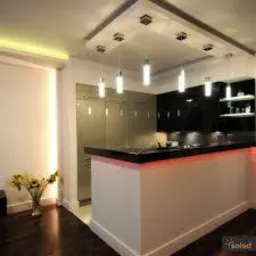 Nowoczesna kuchnia z wyspą i oświetleniem LED podszafkowym. Minimalistyczny design, ciepłe światło, bukiet kwiatów na blacie. Czarny blat, białe ściany.