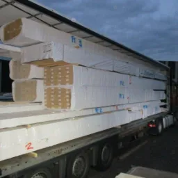 Załadunek drewna konstrukcyjnego KVH i BSH, owiniętego folią, na naczepę ciężarówki, widoczne oznaczenia 'Pz 3' i 'R2' na paczkach.