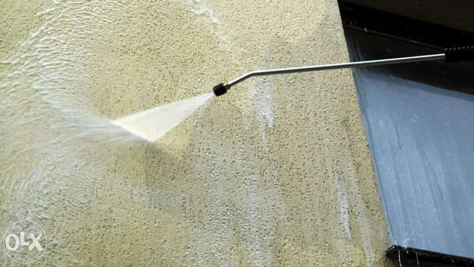 Czyszczenie elewacji budynku za pomocą myjki ciśnieniowej. Strumień wody usuwa zabrudzenia z chropowatej powierzchni ściany. Widoczne ślady czyszczenia.