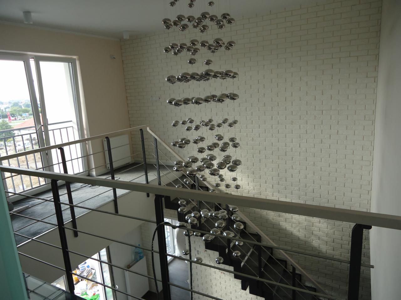 Nowoczesne schody z metalowymi balustradami i oryginalną lampą wiszącą na tle ściany z białej cegły, widok z góry.