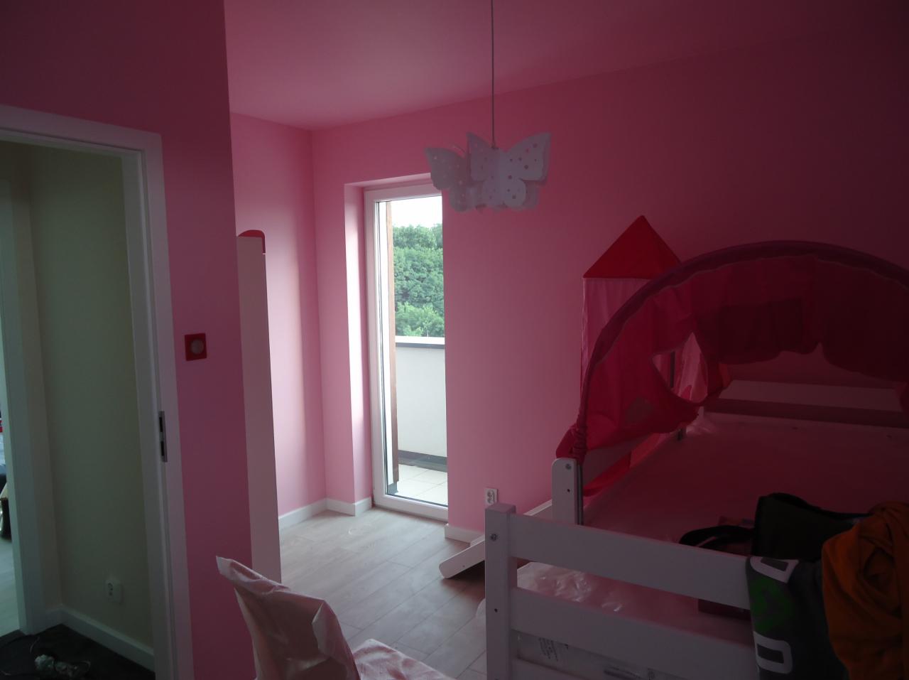 Różowy pokój dziecięcy po malowaniu: ściany, sufit,  drzwi. Widoczny fragment łóżka z baldachimem i lampa w kształcie motyla. Jasne panele na podłodze.