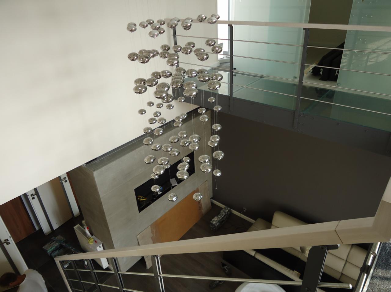 Nowoczesne wnętrze z designerską lampą kulkową, widok z góry na salon z kominkiem i szklaną balustradą. Minimalistyczny styl, jasne ściany i drewniana podłoga.