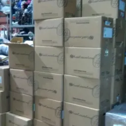 Kartonowe pudełka z logo firmy ustawione na palecie w magazynie odzieży używanej, w tle regały z ubraniami.