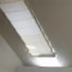 Okno dachowe z wewnętrzną przesłoną materiałową w kolorze białym, częściowo zasłoniętą, widoczne w jasnym wnętrzu.