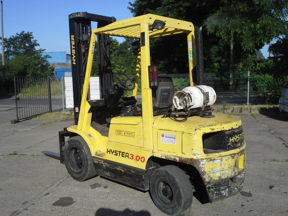 Używany wózek widłowy Hyster H3.00XMX z butlą LPG, widoczne ślady eksploatacji na karoserii, zaparkowany na betonowym placu w słoneczny dzień.
