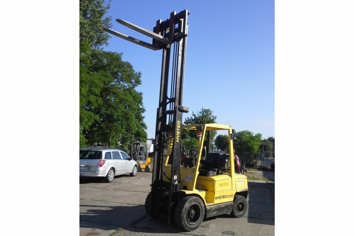 Używany wózek widłowy Hyster H3.00XMX, rok produkcji 2001, z podniesionymi widłami, widoczny na zewnątrz w słoneczny dzień, zarys drzew w tle.