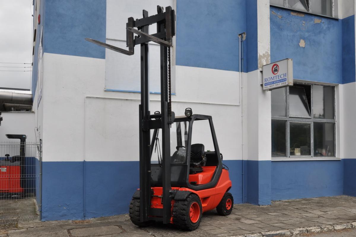 Pomarańczowy wózek widłowy Linde H30T z czarną konstrukcją masztu stoi przed budynkiem z niebiesko-białymi pasami, widoczny szyld firmy Romtech nad oknem.