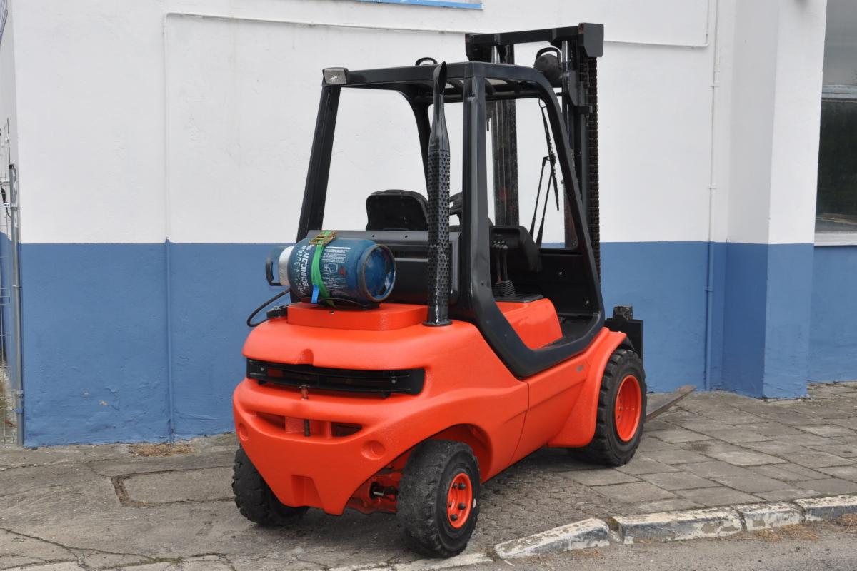 Pomarańczowy wózek widłowy Linde H30T z butlą LPG na tle budynku z niebiesko-białą elewacją.