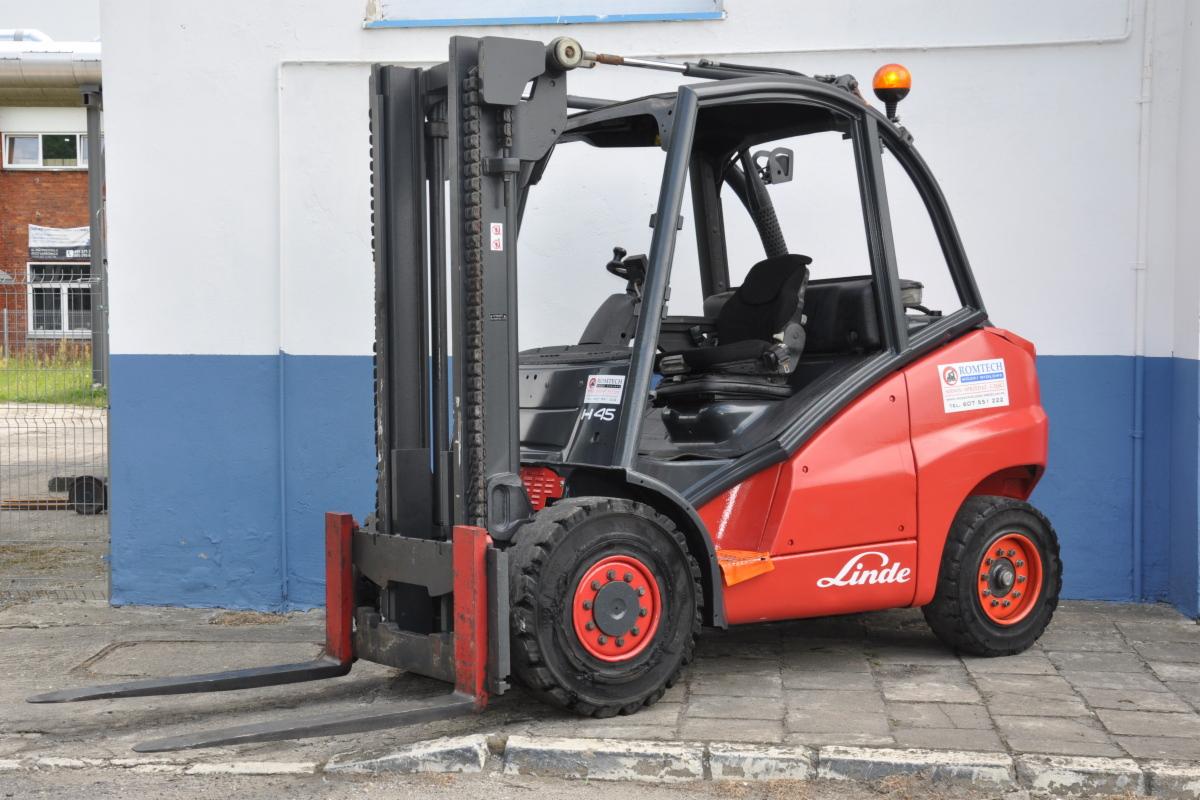 Czerwony wózek widłowy Linde H45 z czarną kabiną i pomarańczowym światłem ostrzegawczym, stojący na betonowej nawierzchni przed budynkiem z niebiesko-białą ścianą.