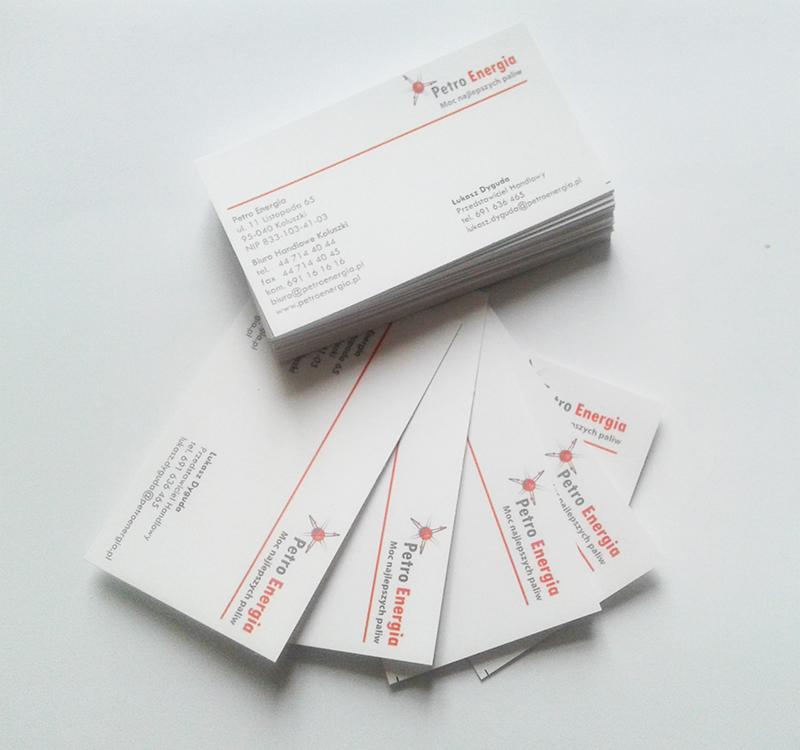 Stos wizytówek Petro Energia z danymi kontaktowymi i logo, kilka wizytówek rozłożonych obok, jasne tło, stonowana kolorystyka.