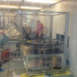 WARM-DOM SP. Z O.O. - Pracownicy w kombinezonach i kaskach obsługują maszynę w sterylnym pomieszczeniu, prawdopodobnie podczas montażu lub konserwacji.