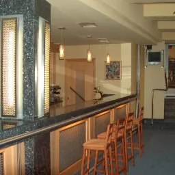 Wykończony bar z kamiennym blatem i oświetleniem w lokalu w Warszawie, widoczne krzesła barowe i schody.