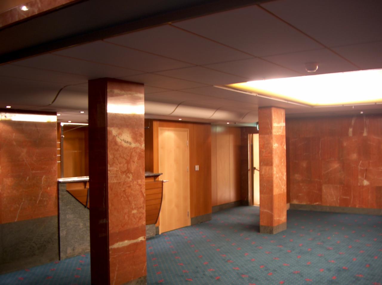 Wnętrze biura z marmurowymi kolumnami, drewnianą boazerią i niebieską wykładziną dywanową w czerwone wzory.