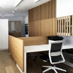 Nowoczesne biuro z drewnianymi panelami działowymi, białymi meblami i ergonomicznym krzesłem biurowym, drukarka na biurku.