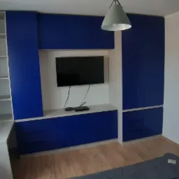 Niebieska zabudowa meblowa z szafkami, półkami i miejscem na telewizor w salonie w Słupsku, z widoczną lampą wiszącą i zasłoniętym oknem.