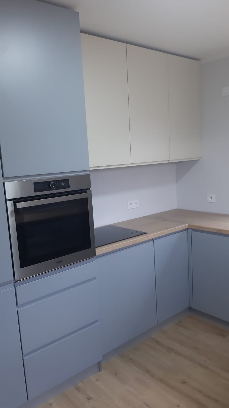 Nowoczesna kuchnia w odcieniach szarości i beżu z wbudowanym piekarnikiem i płytą grzewczą, minimalistyczne fronty szafek bez uchwytów, jasna drewniana podłoga.