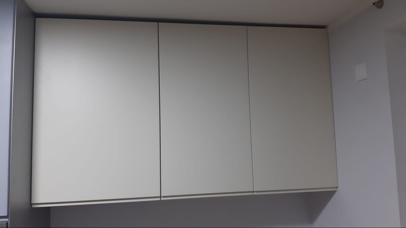 Trzy górne szafki kuchenne w kolorze jasnego beżu, z minimalistycznymi uchwytami, zamontowane na ścianie w kuchni.