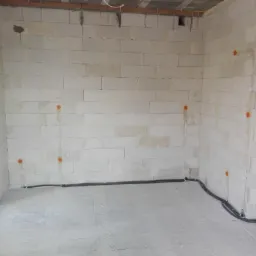 Surowy stan wnętrza z instalacją elektryczną: widoczne przewody w ścianach z betonu komórkowego i rurki instalacyjne pod sufitem.
