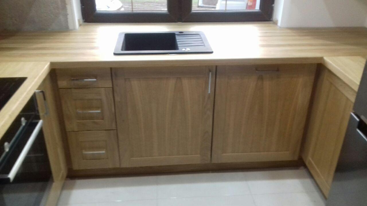 Fragment zabudowy kuchennej z drewnianymi szafkami, blatem z widocznym usłojeniem i czarnym zlewem pod oknem.