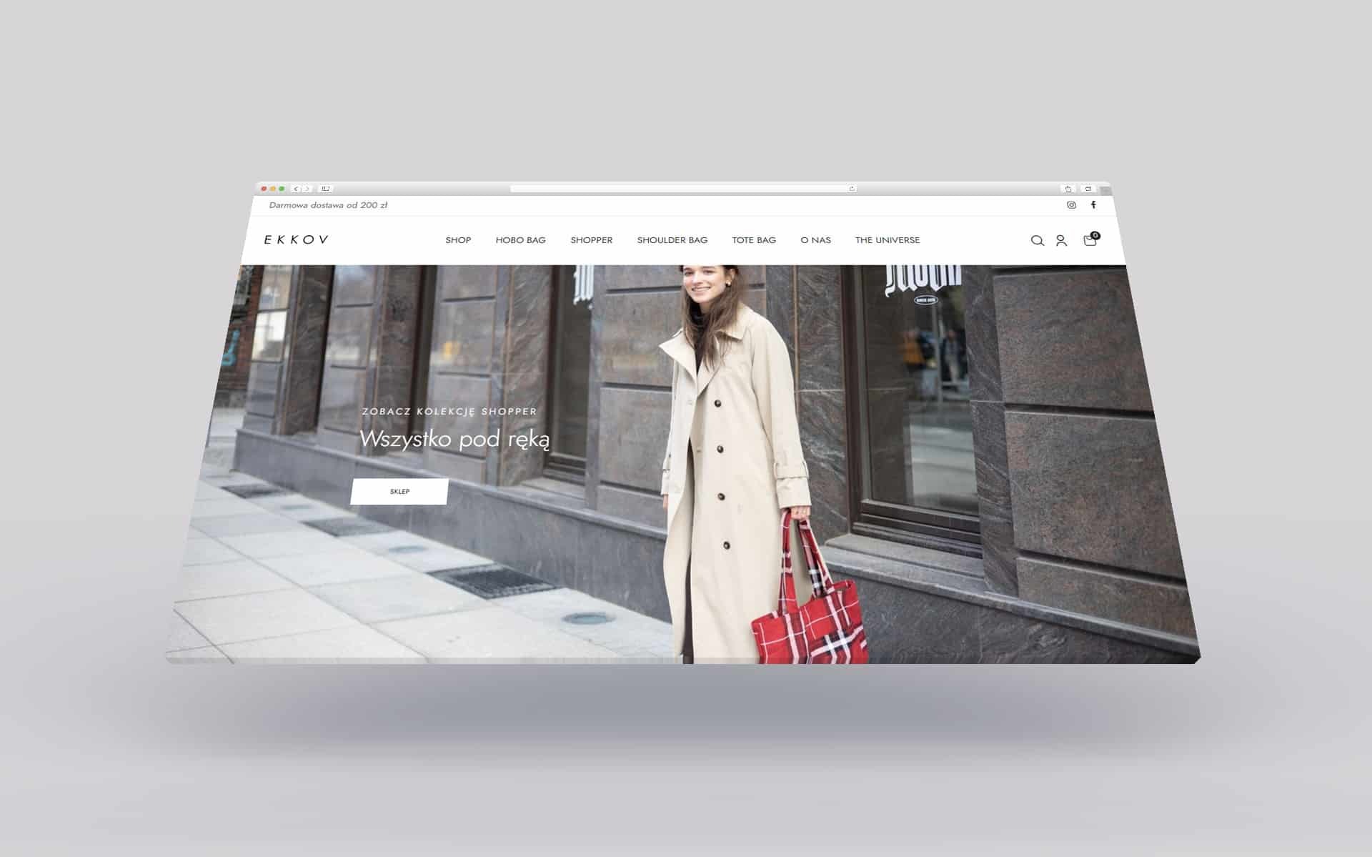 Ekran laptopa prezentujący stronę internetową sklepu odzieżowego EKKOV z modelką w płaszczu i torbą shopper. Widoczne menu nawigacyjne, logo oraz hasło reklamowe 'Wszystko pod ręką'.