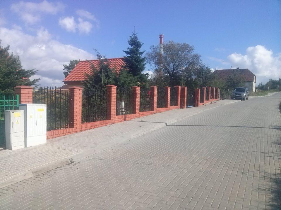 Murowane ogrodzenie z cegły klinkierowej i elementami metalowymi w Zgorzelcu. Widok na posesję i ulicę. Słupki ogrodzeniowe z daszkami.