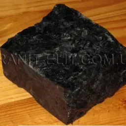 Czarny, surowy blok kostki granitowej o nieregularnych krawędziach, leżący na drewnianej powierzchni. Widoczne delikatne refleksy światła na powierzchni kamienia.